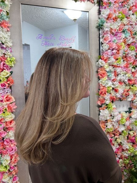 A woman is standing in front of a mirror in front of a wall of flowers.