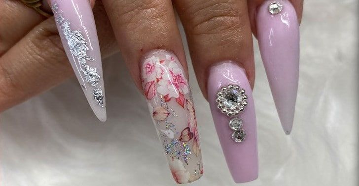 A close up of a woman 's nails with a floral design and rhinestones.