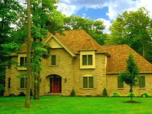 A large brick house with a red door is surrounded by trees and grass.