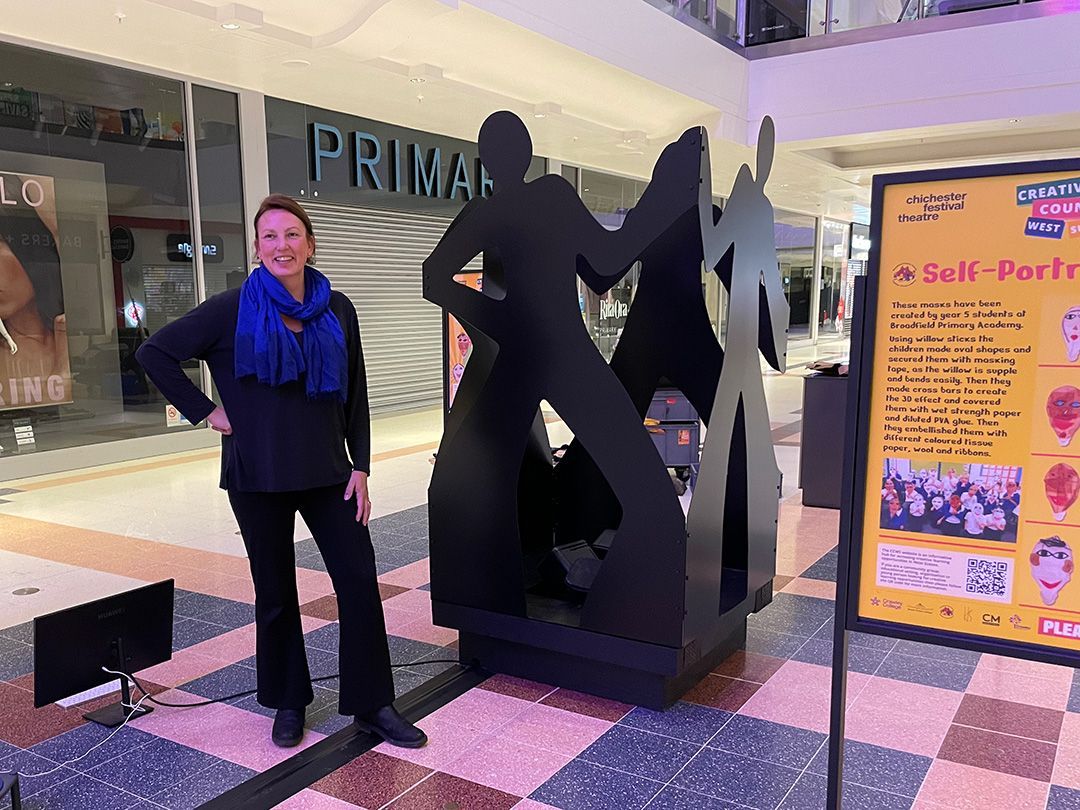 A woman is standing next to a metal sculpture of a man in a mall.