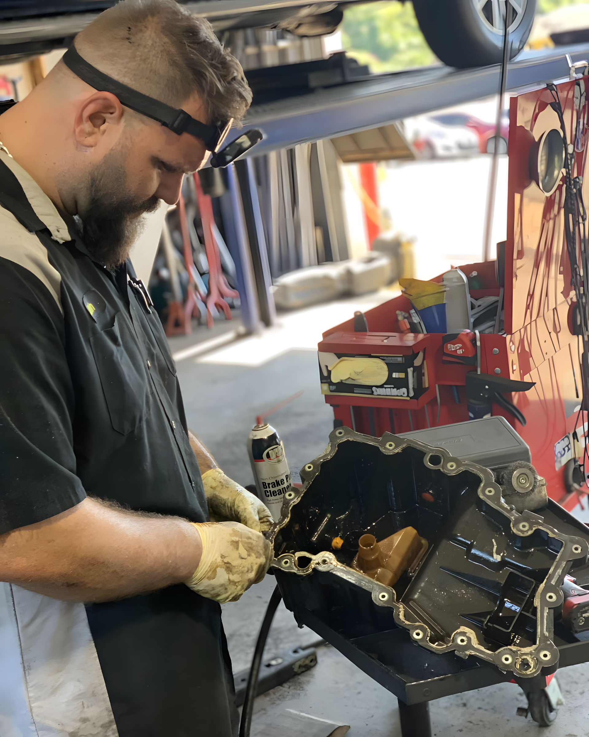 Mechanic working on car engine, wearing a headlamp, outdoors, next to car lift. | Total Automotive