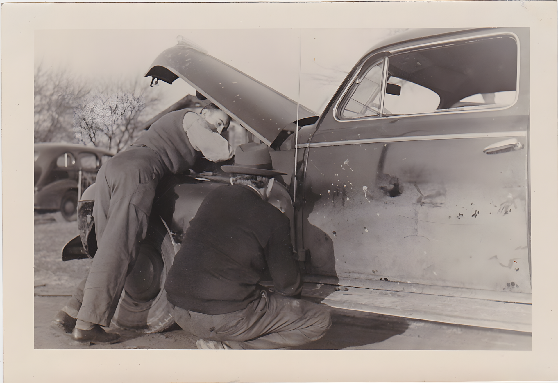 Two men working on a car with the hood up, roadside. Black and white photograph. | Total Automotive