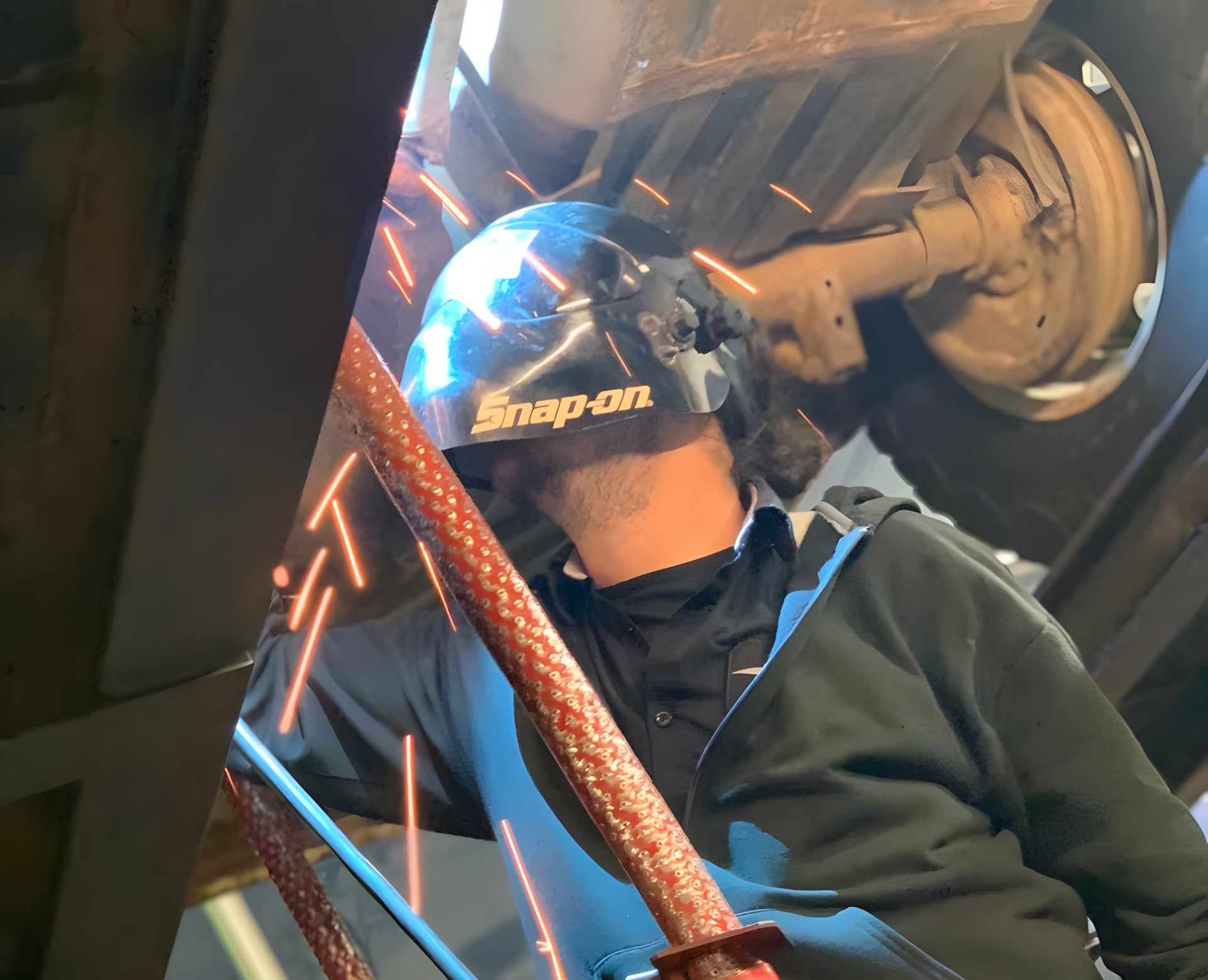 Person welding underneath a vehicle, wearing a welding helmet, with sparks visible. | Total Automotive