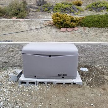 A kohler generator is sitting on top of a concrete block in the dirt.