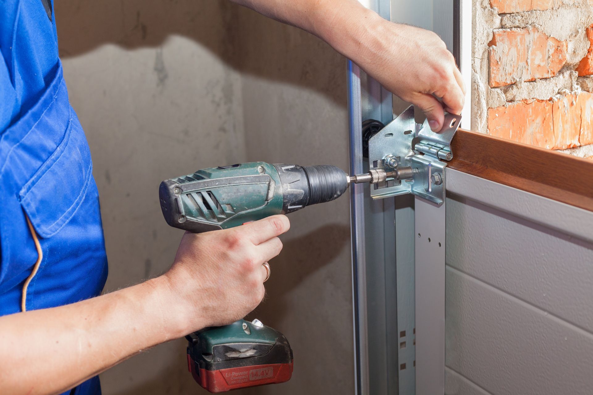 A garage door repair technician is using a drill to fix a track bracket.