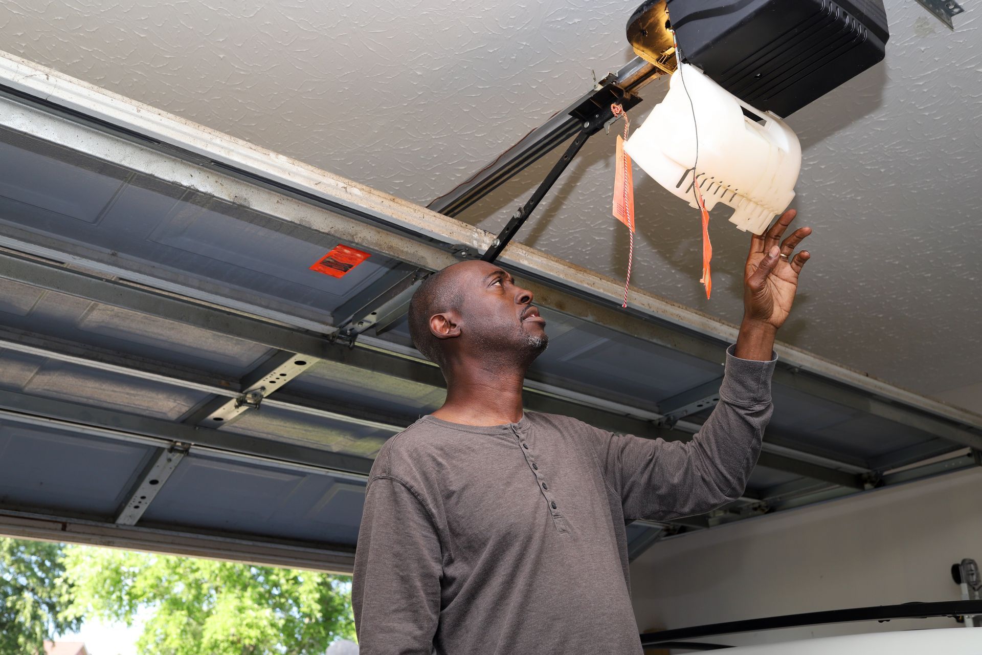 Technician inspecting opener motor during overhead garage door repairs inside a residential garage.