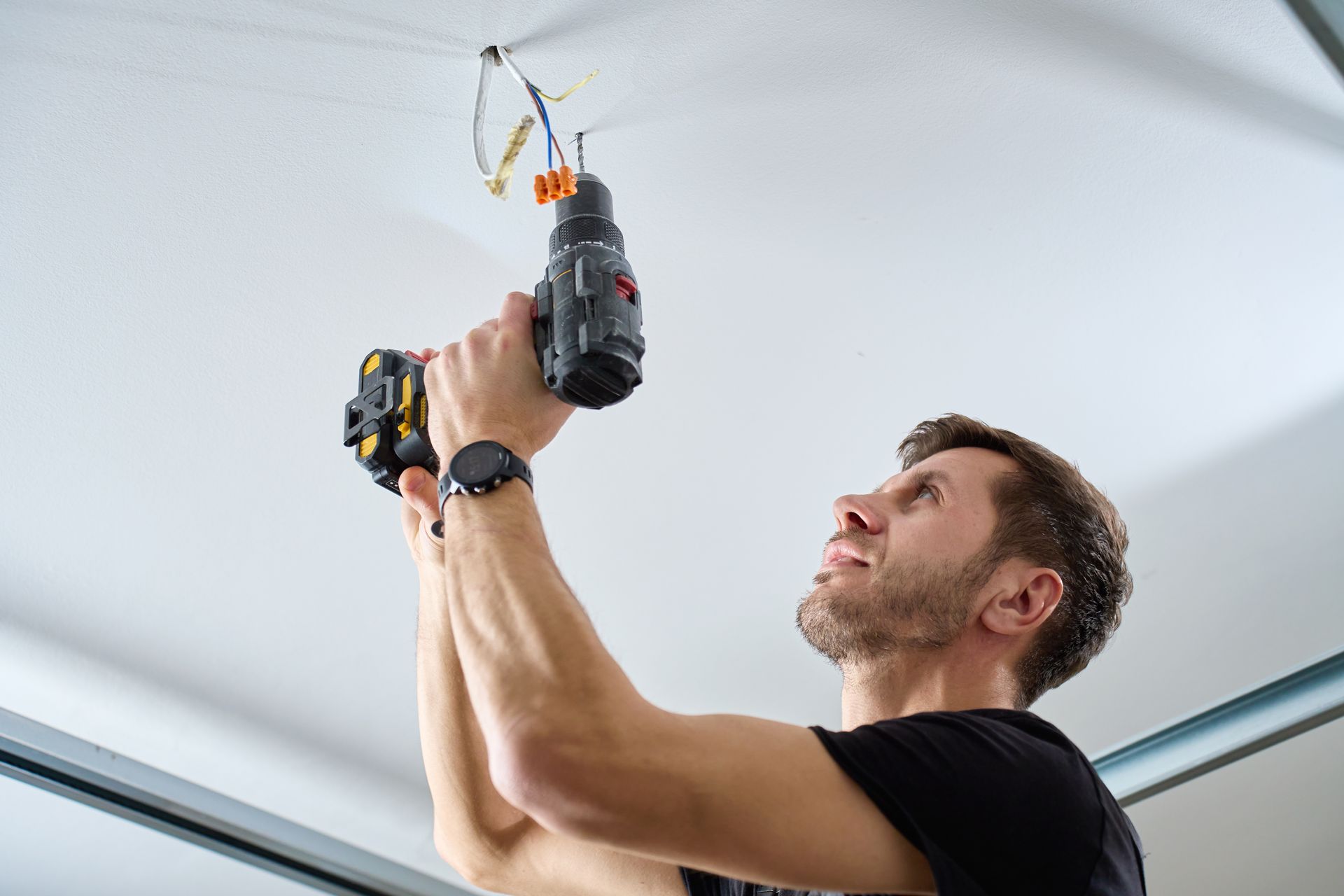 Man using a drill on a ceiling, near exposed wires, indoors.