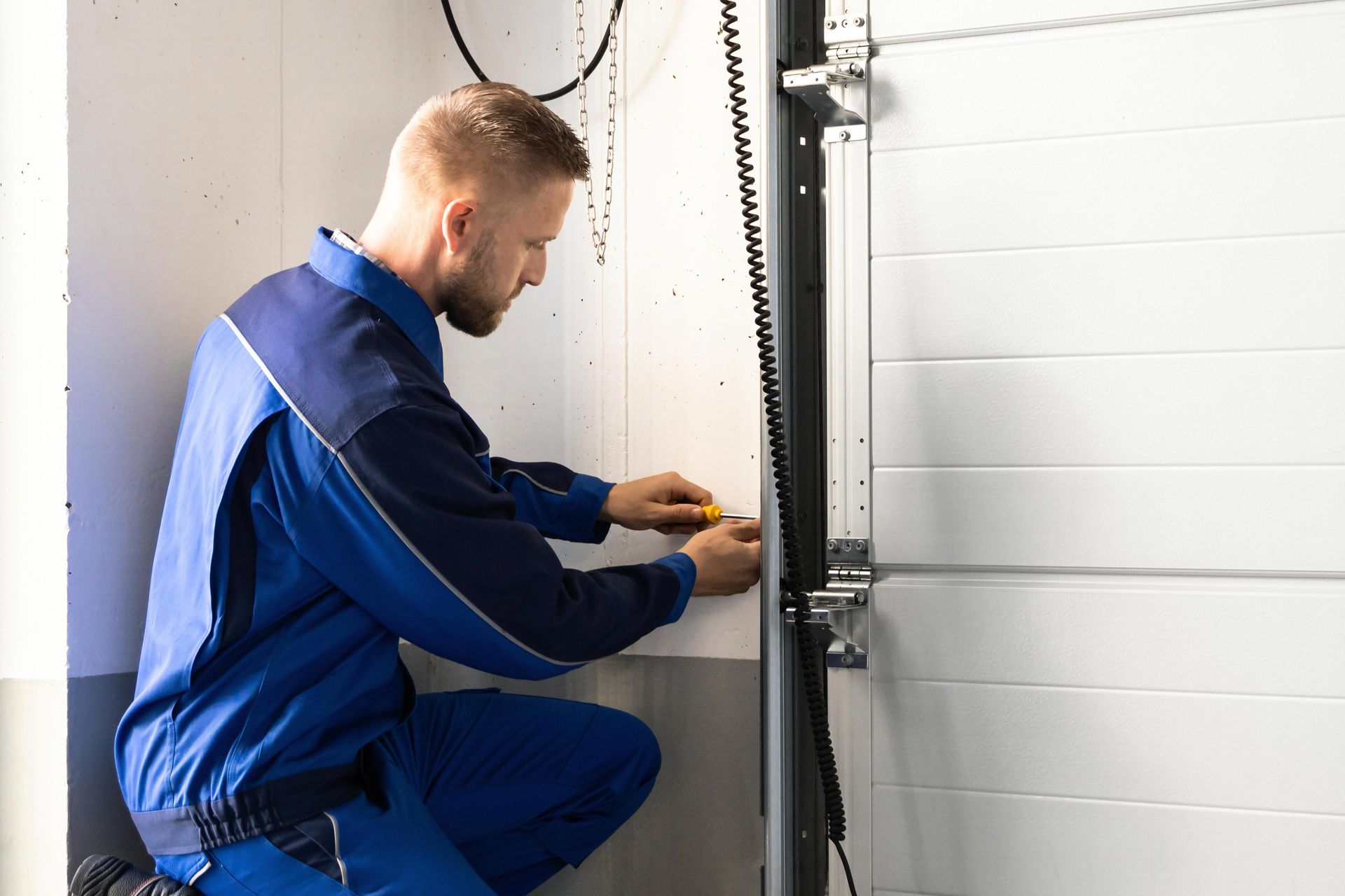 Mechanic in blue coveralls fixing a white garage door with a screwdriver. Mechanic in blue coveralls fixing a white garage door with a screwdriver.