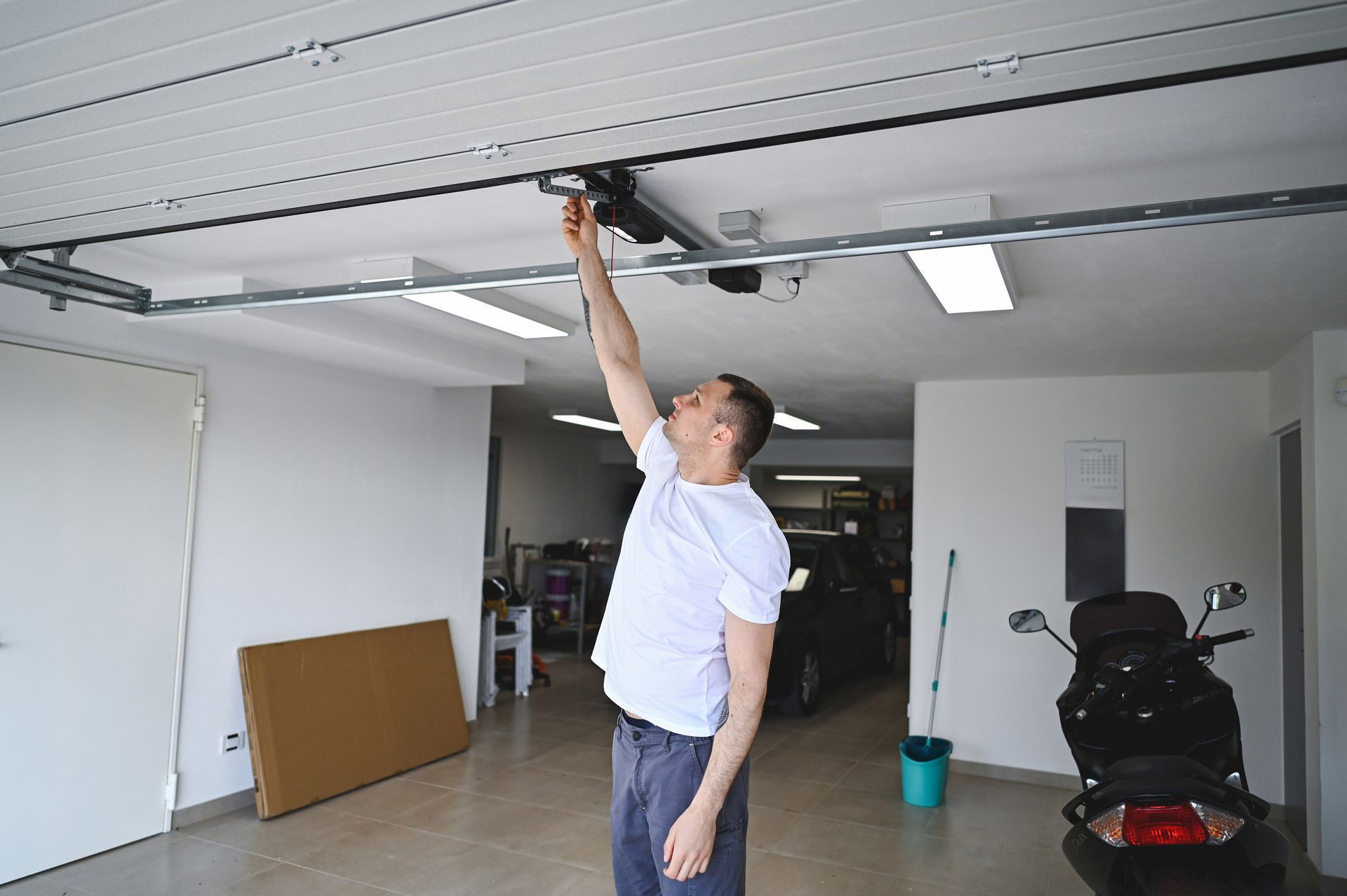 Man in garage reaching up to garage door opener.