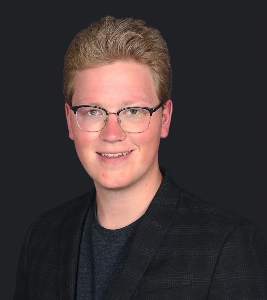 A young man wearing glasses and a suit is smiling for the camera.