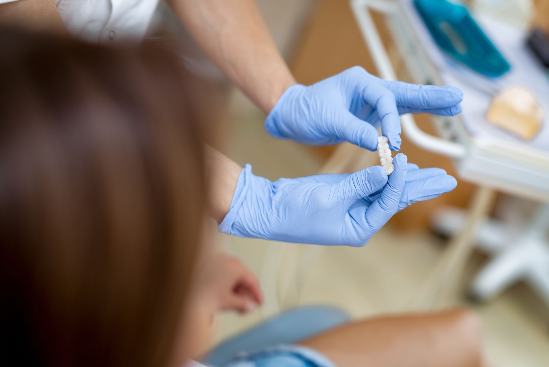 Gloved hands holding a small vial in a medical setting, with a blurred patient in the foreground Gloved hands holding a small vial in a medical setting, with a blurred patient in the foreground