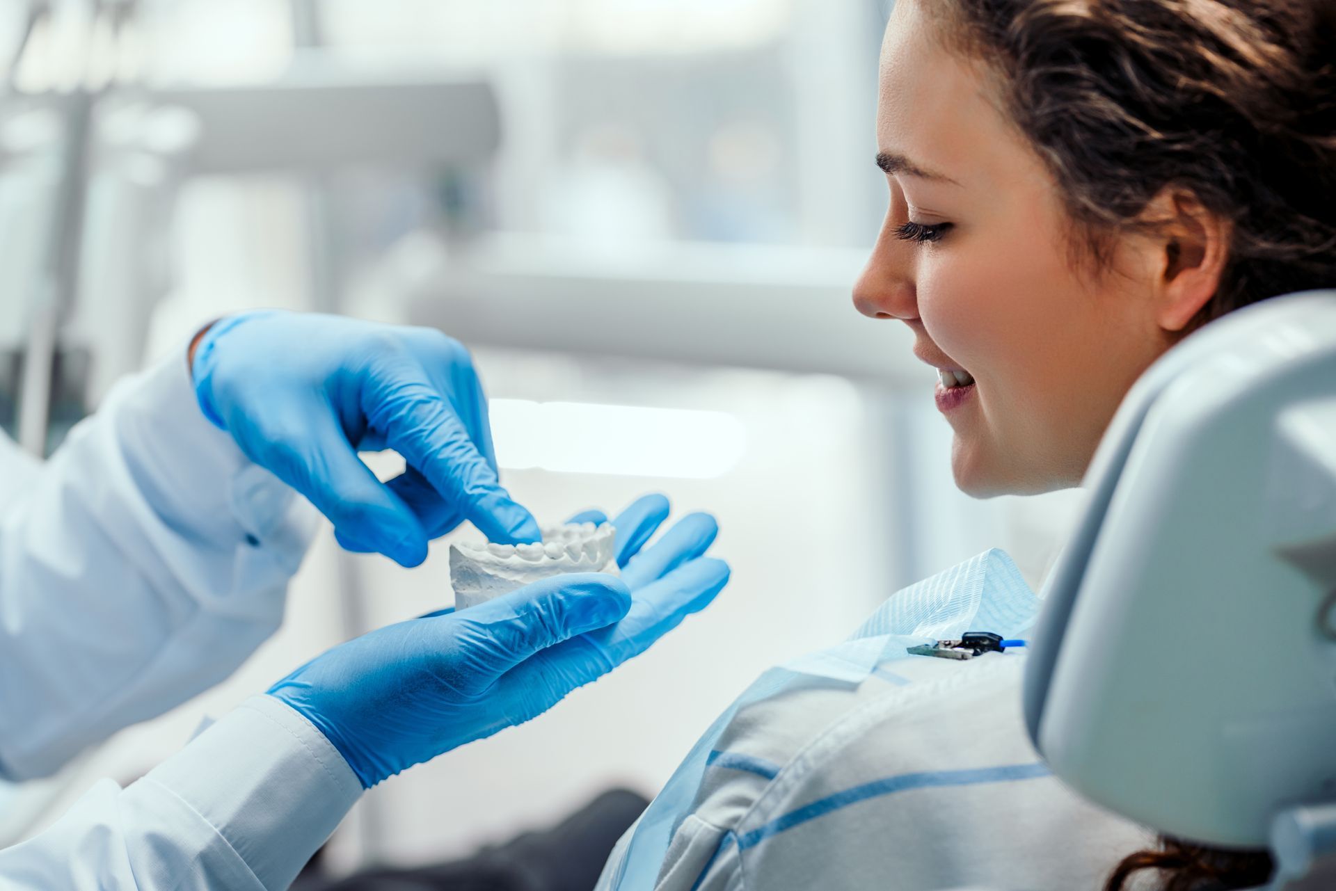 Dental professional in blue gloves examining a patient in a clinic, with the patient smiling and reclined. Dental professional in blue gloves examining a patient in a clinic, with the patient smiling and reclined.