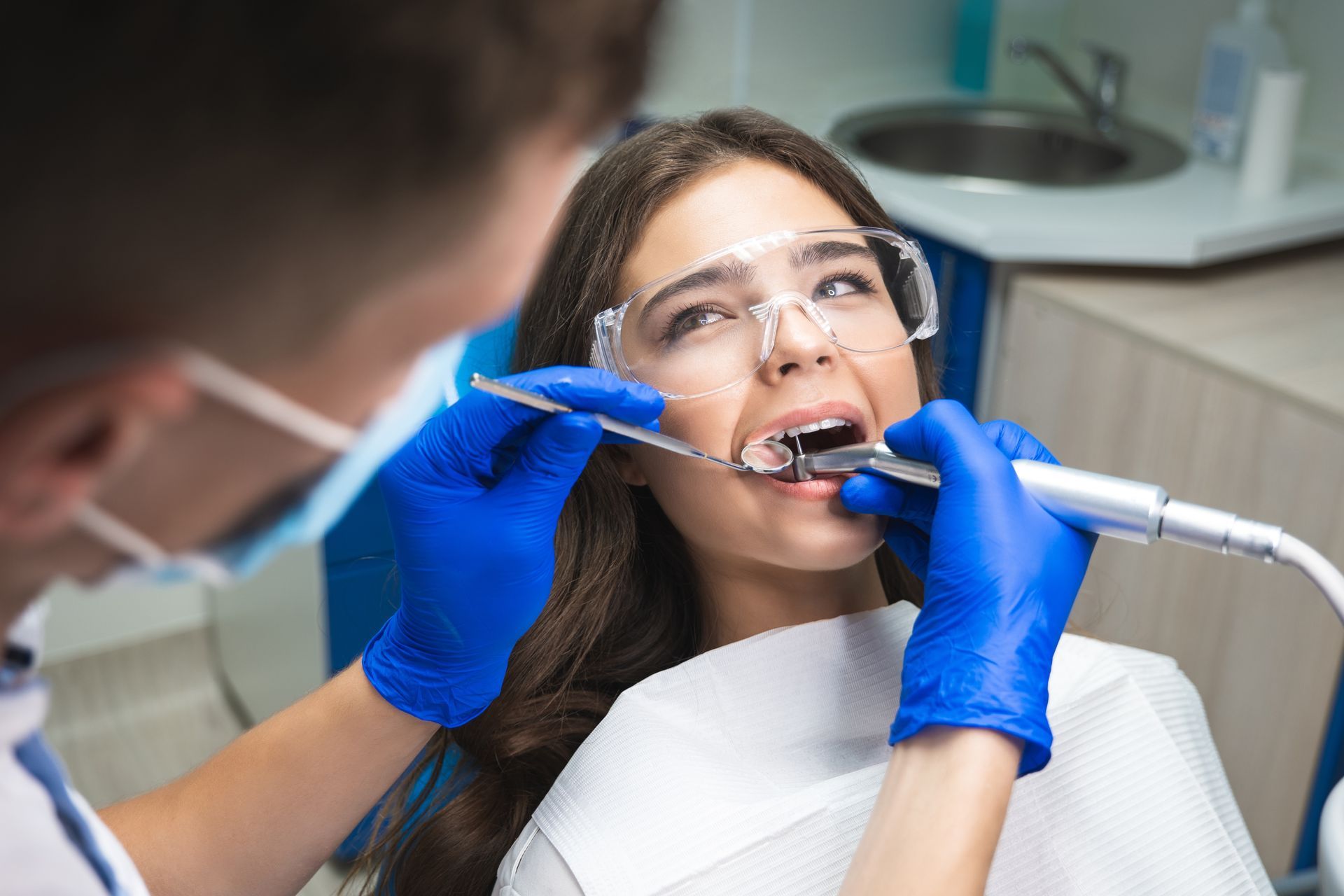 Dentist treating a patient with a drill, patient wearing protective glasses and mouth open in a dental clinic Dentist treating a patient with a drill, patient wearing protective glasses and mouth open in a dental clinic