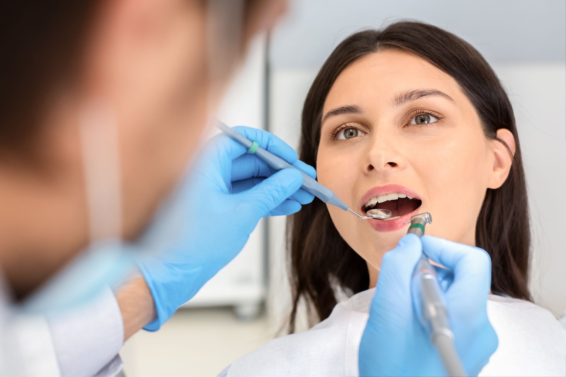 Dentist examining a patient’s open mouth with gloved hands and dental tools Dentist examining a patient’s open mouth with gloved hands and dental tools