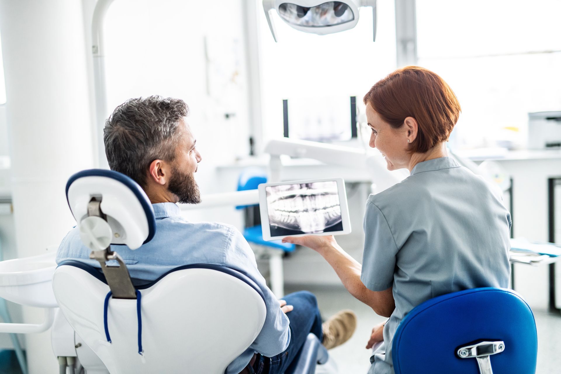 Dentist showing X-rays to a patient seated in a dental chair during a consultation Dentist showing X-rays to a patient seated in a dental chair during a consultation