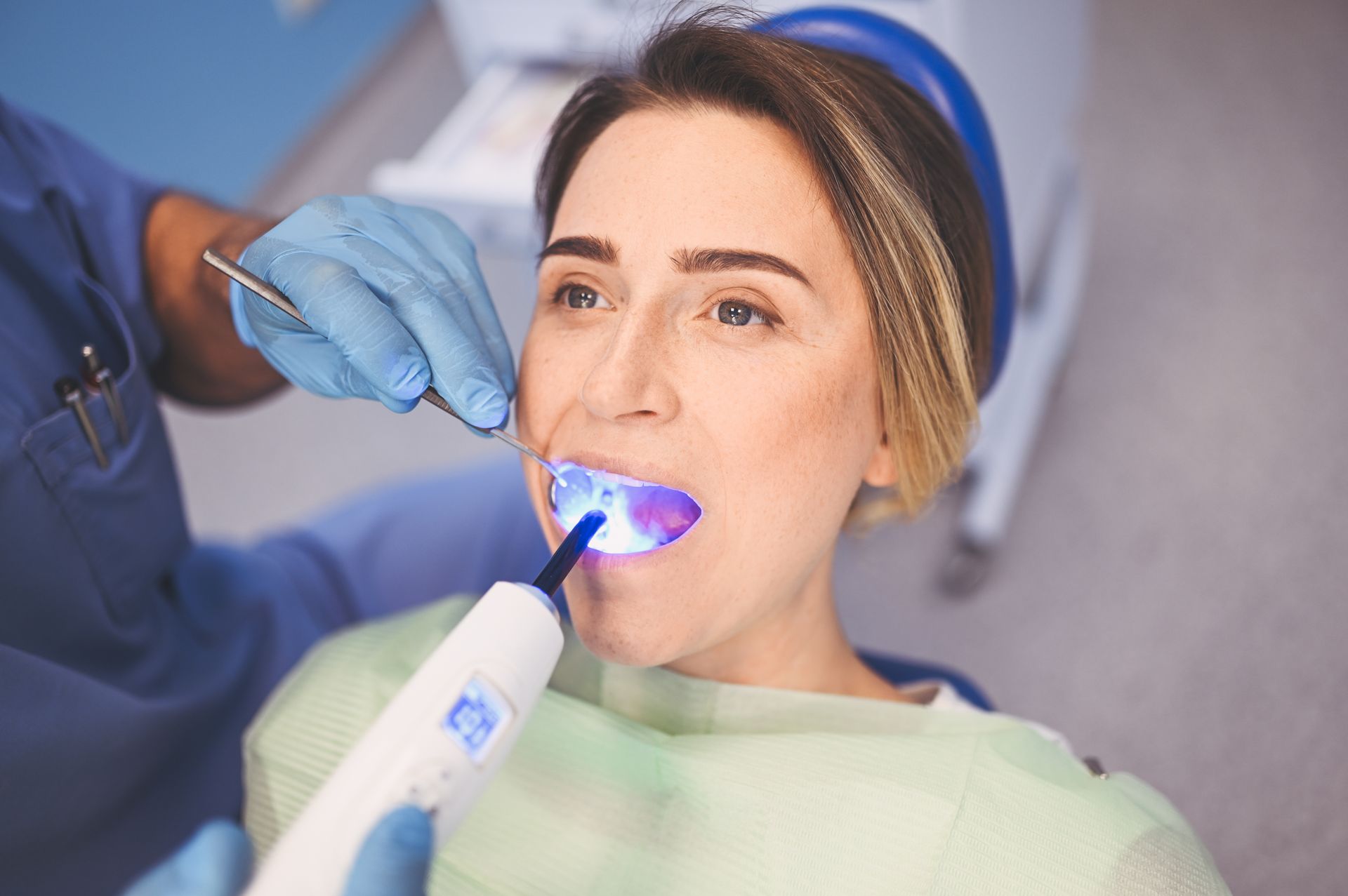 Dentist using a blue curing light on a patient wearing a cheek retractor during a dental procedure Dentist using a blue curing light on a patient wearing a cheek retractor during a dental procedure