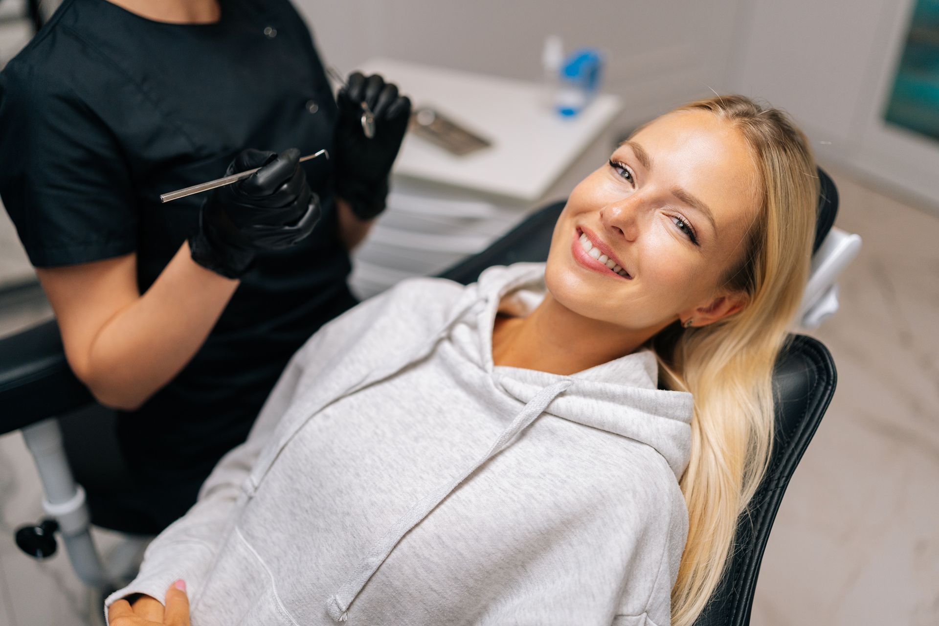 Woman smiling in a dental chair during a checkup with a clinician nearby Woman smiling in a dental chair during a checkup with a clinician nearby