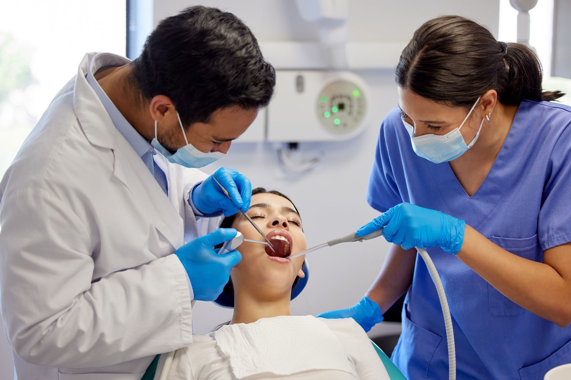 Dentist and assistant treating a patient in a dental clinic, using tools while the patient lies back in a chair. Dentist and assistant treating a patient in a dental clinic, using tools while the patient lies back in a chair.