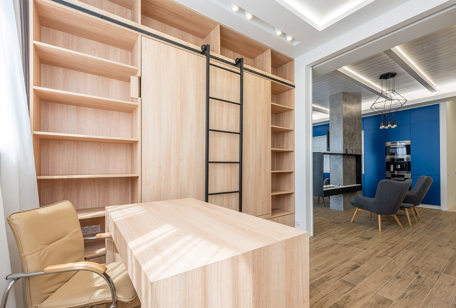A room with a desk , chairs , shelves and a ladder.