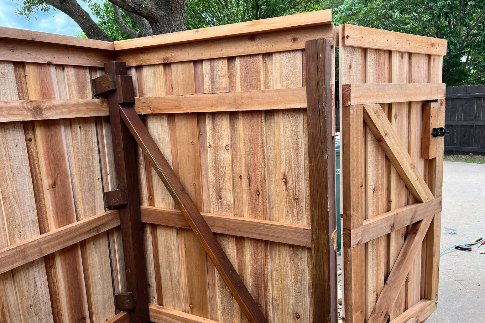 A wooden fence with a gate that is open and a tree in the background.