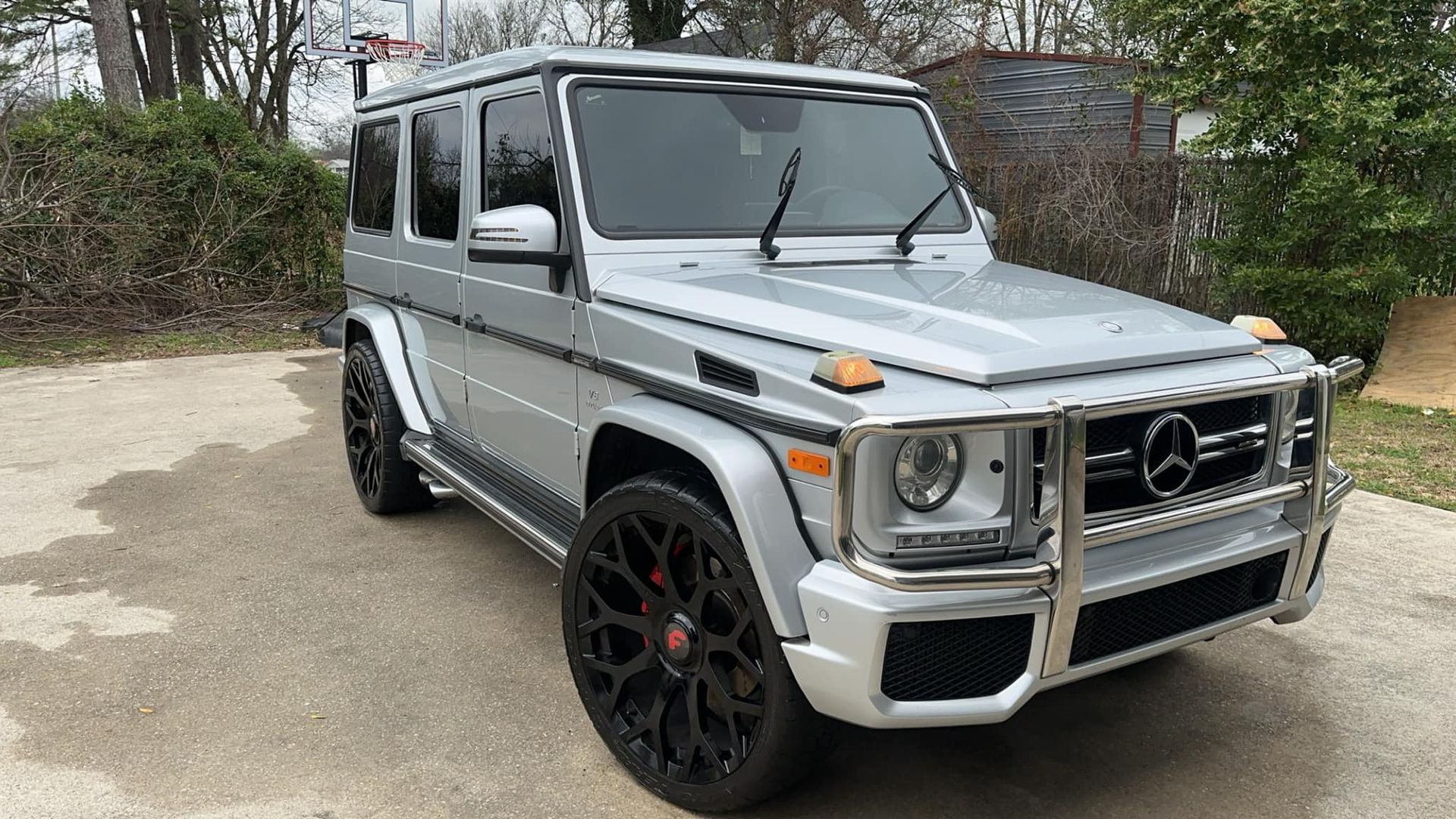 A silver mercedes benz g63 is parked in a driveway.