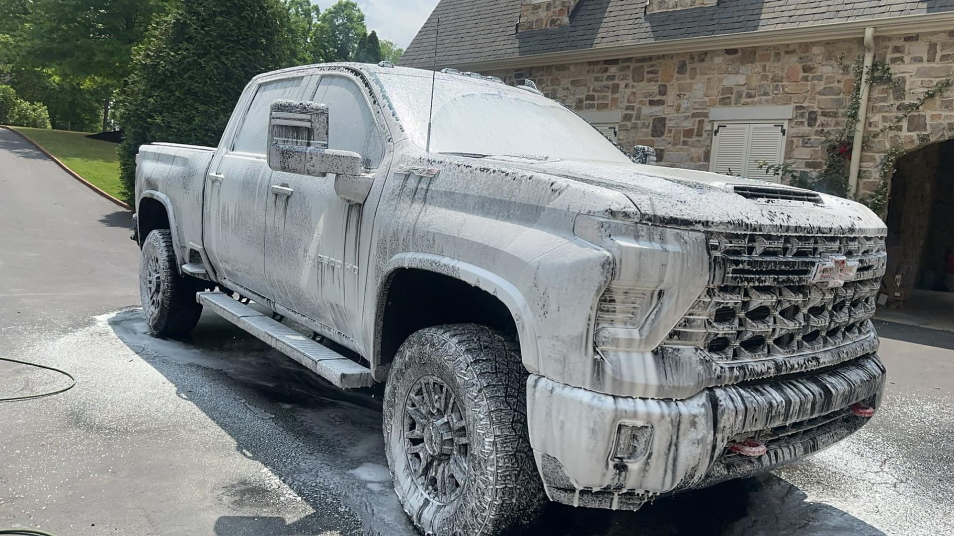 A white truck covered in foam is parked in front of a stone building.