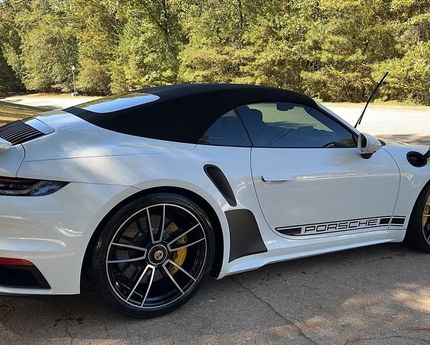 A white sports car with a black top is parked in a driveway.