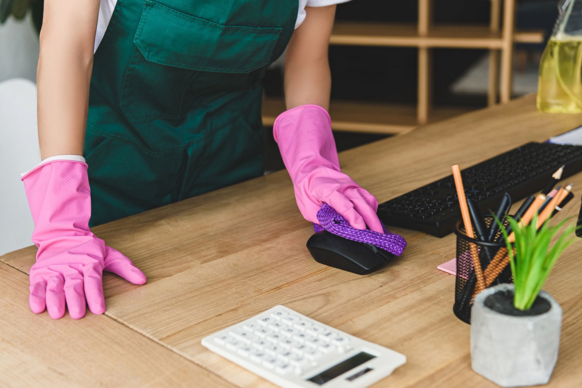 A woman wearing pink gloves is cleaning a desk with a sponge.