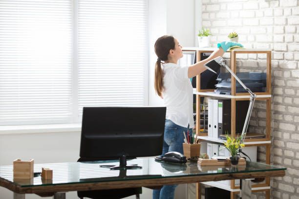 A woman is cleaning a shelf in an office.