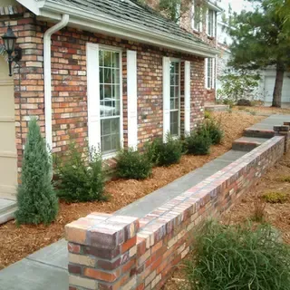Brick house exterior with a brick walkway, shrubs, and windows.