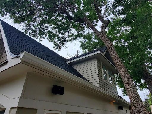 A building with a dark roof, light siding, and a large tree.
