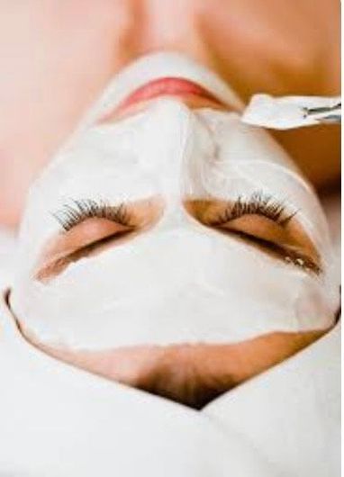Person receiving a facial mask treatment; white cream applied to face with eyes closed.