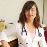 Woman with stethoscope; white jacket, glasses, smiling.