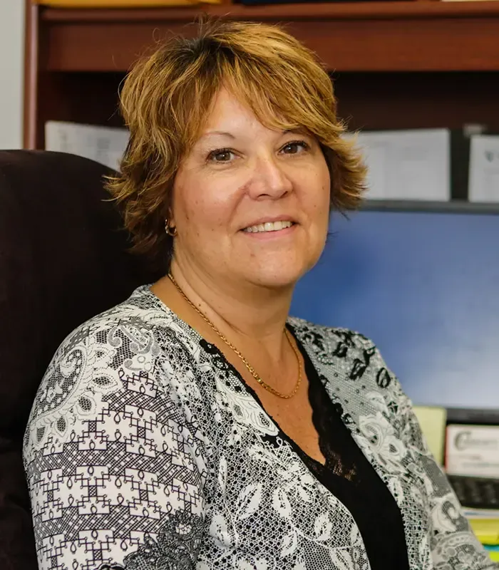 Woman in patterned top, seated at a desk, smiling.