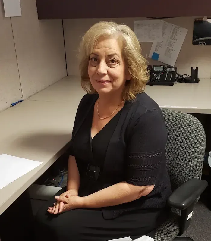 Woman sitting at a desk, wearing black clothing, looking at the camera. Office setting.
