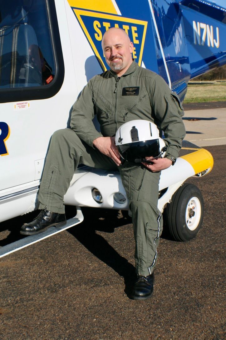 A man is sitting on the side of a helicopter holding a helmet