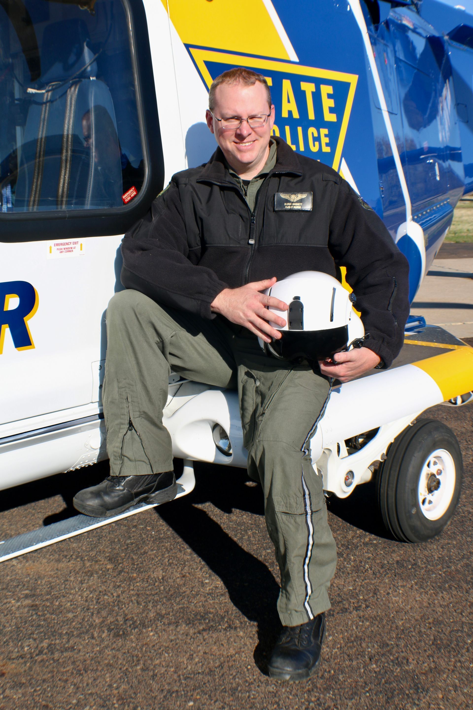 A man is sitting on the side of a helicopter holding a helmet
