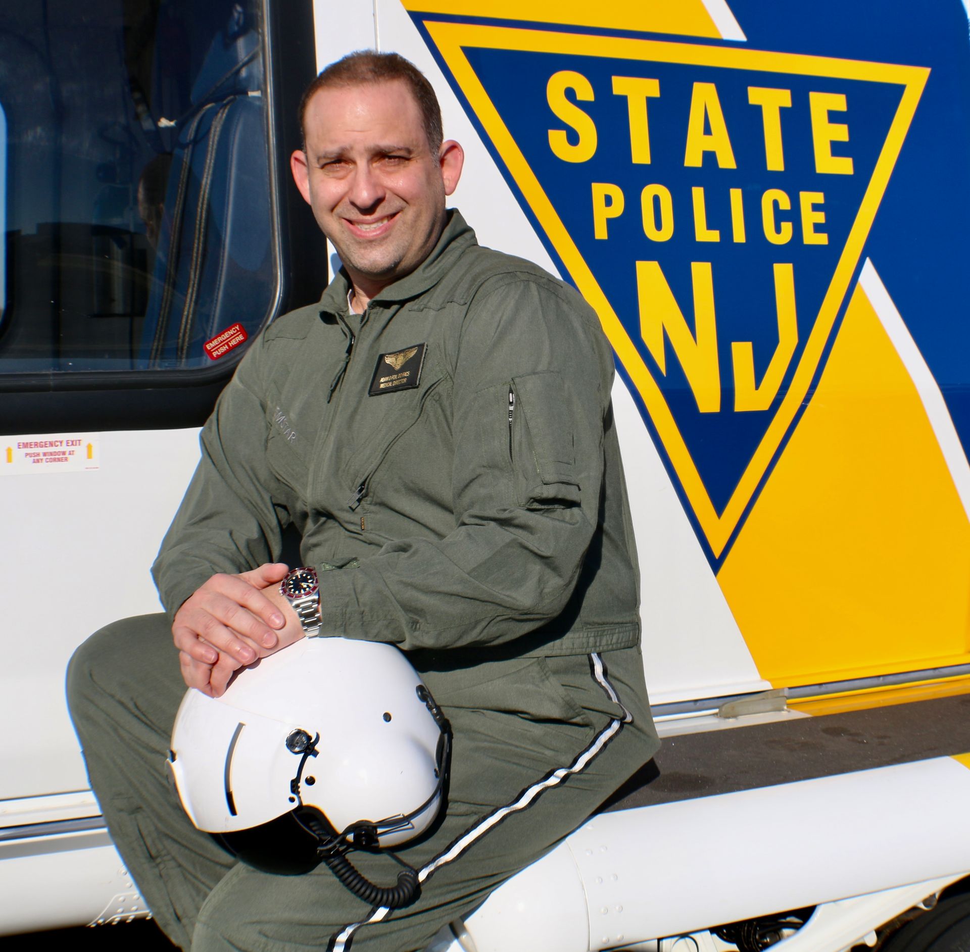 A man sits on the side of a state police vehicle