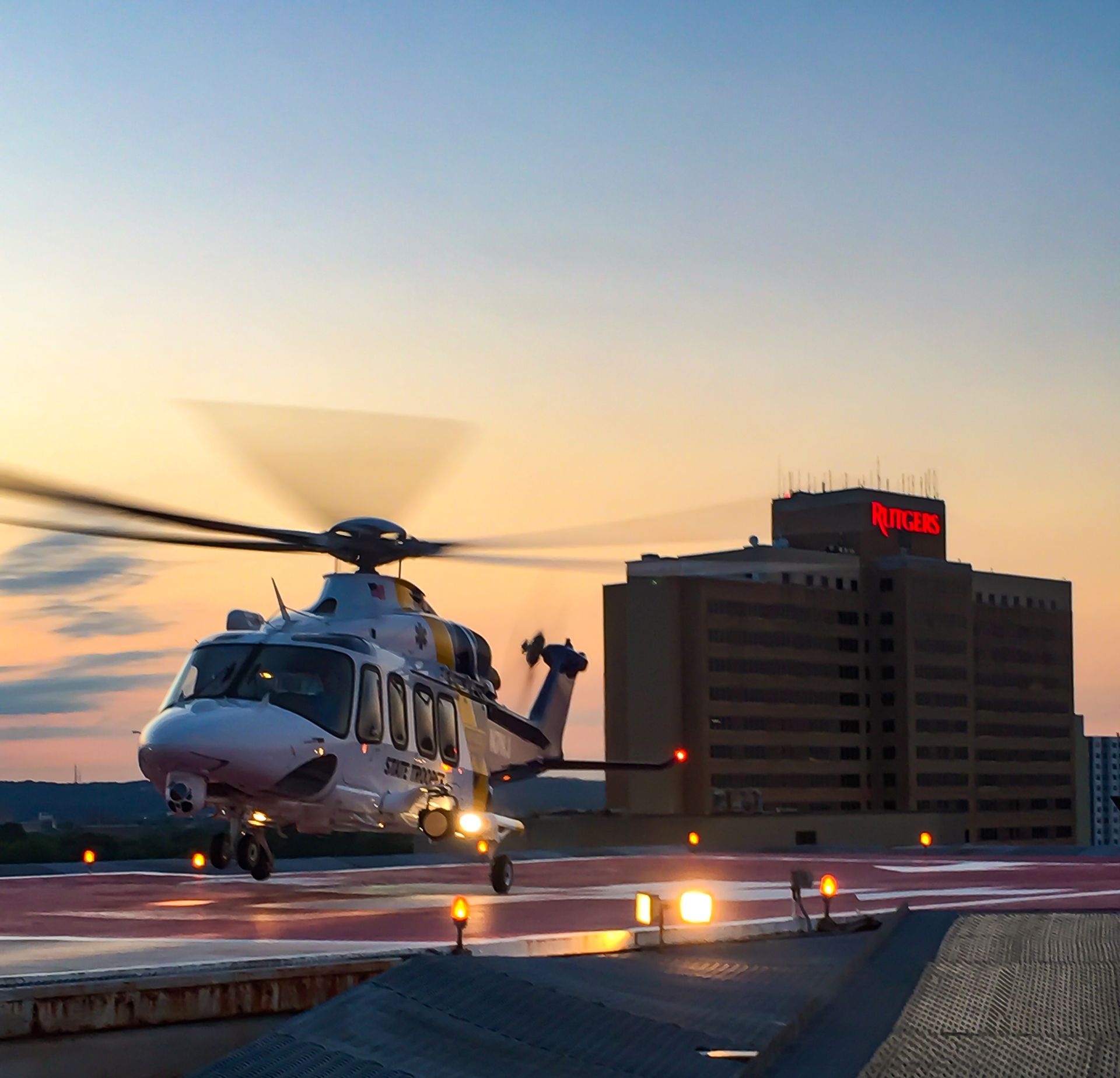 A helicopter is taking off from a runway in front of a building that says ' ryan ' on it