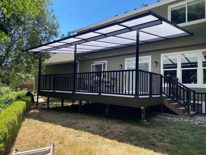 Wooden gazebo with translucent roof, in a wooded area. Interior table and chairs visible.