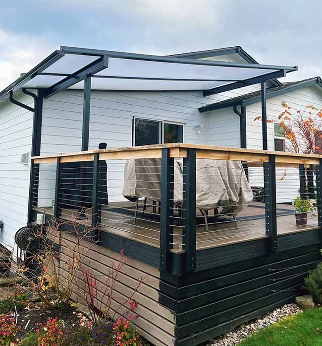 Wooden gazebo with translucent roof, in a wooded area. Interior table and chairs visible.