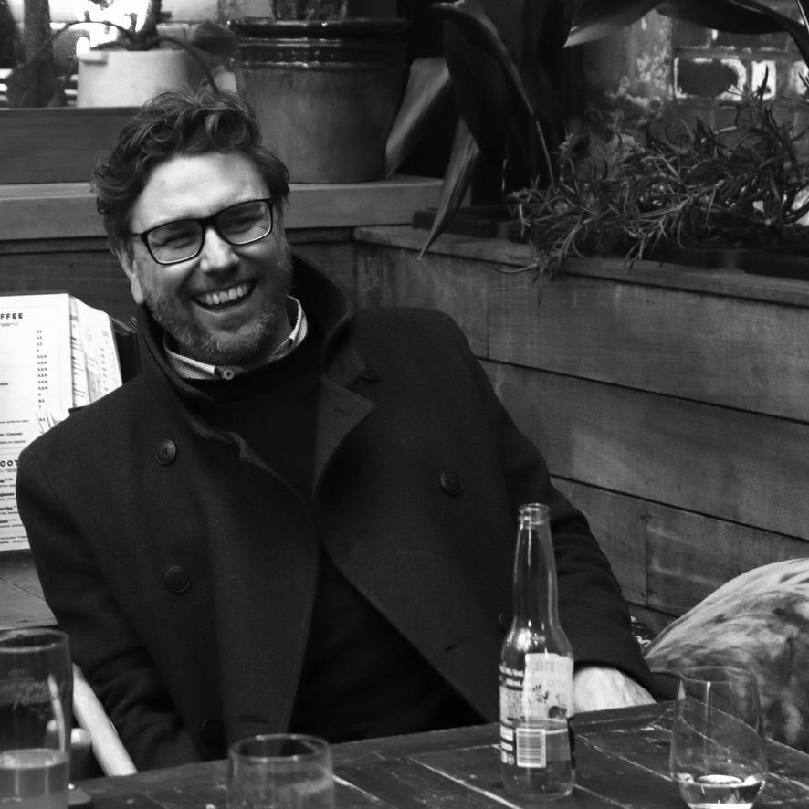 Smiling man in glasses sitting at a café table with a bottle and glasses in front of him