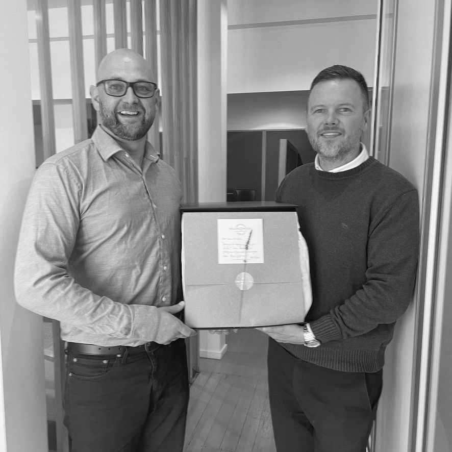 Two men smiling and holding a framed award in an office setting