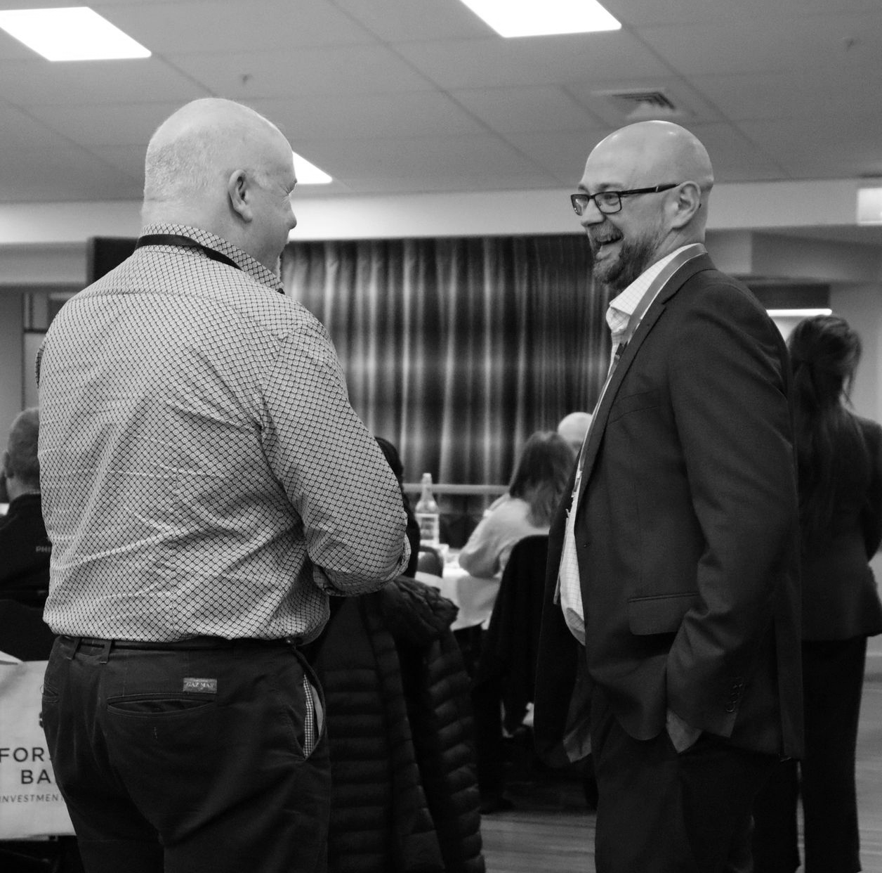 Two men in business attire smiling and talking at a conference or networking event
