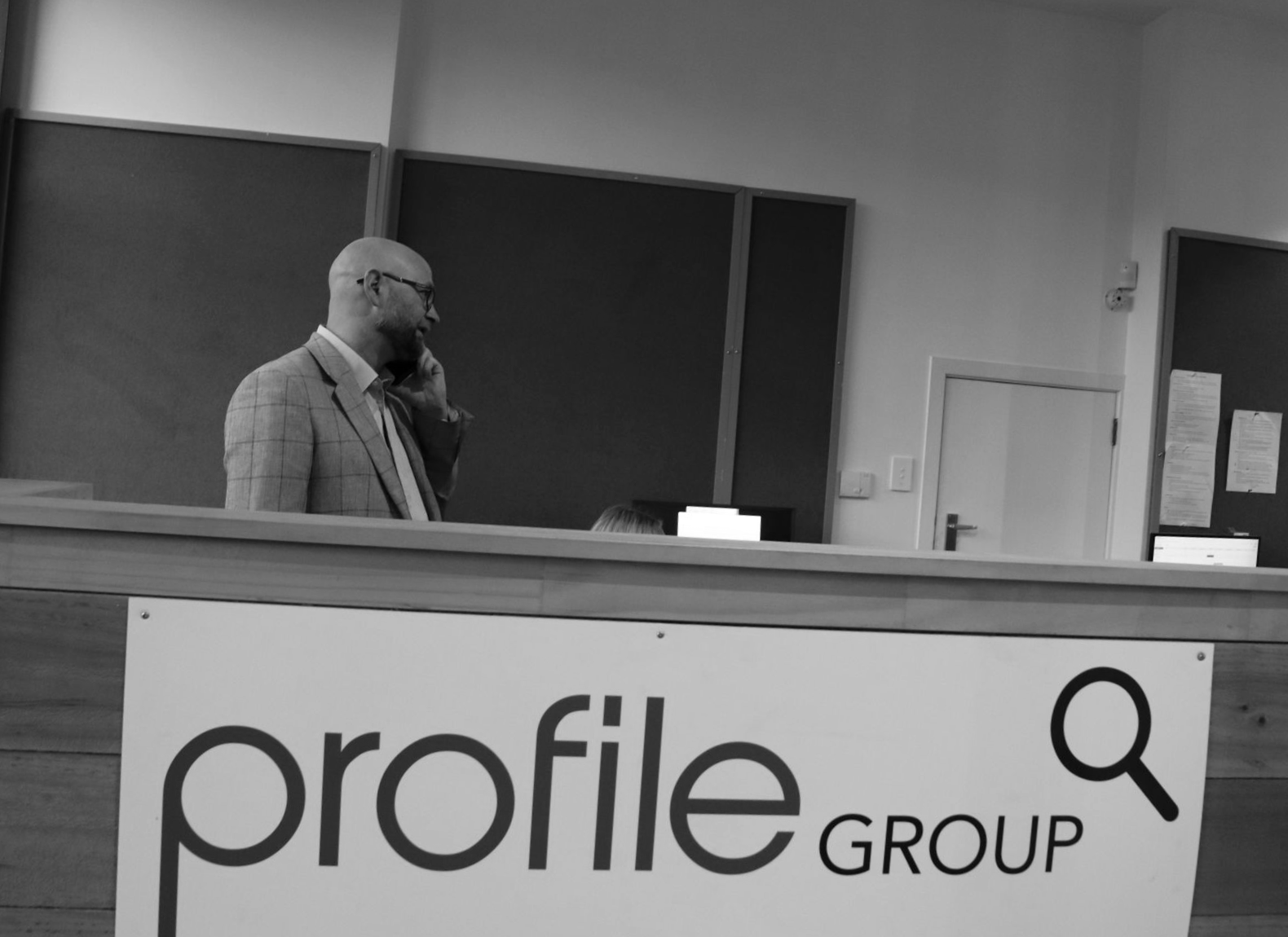 Man standing behind a wooden podium with a Profile Group banner in a lecture hall