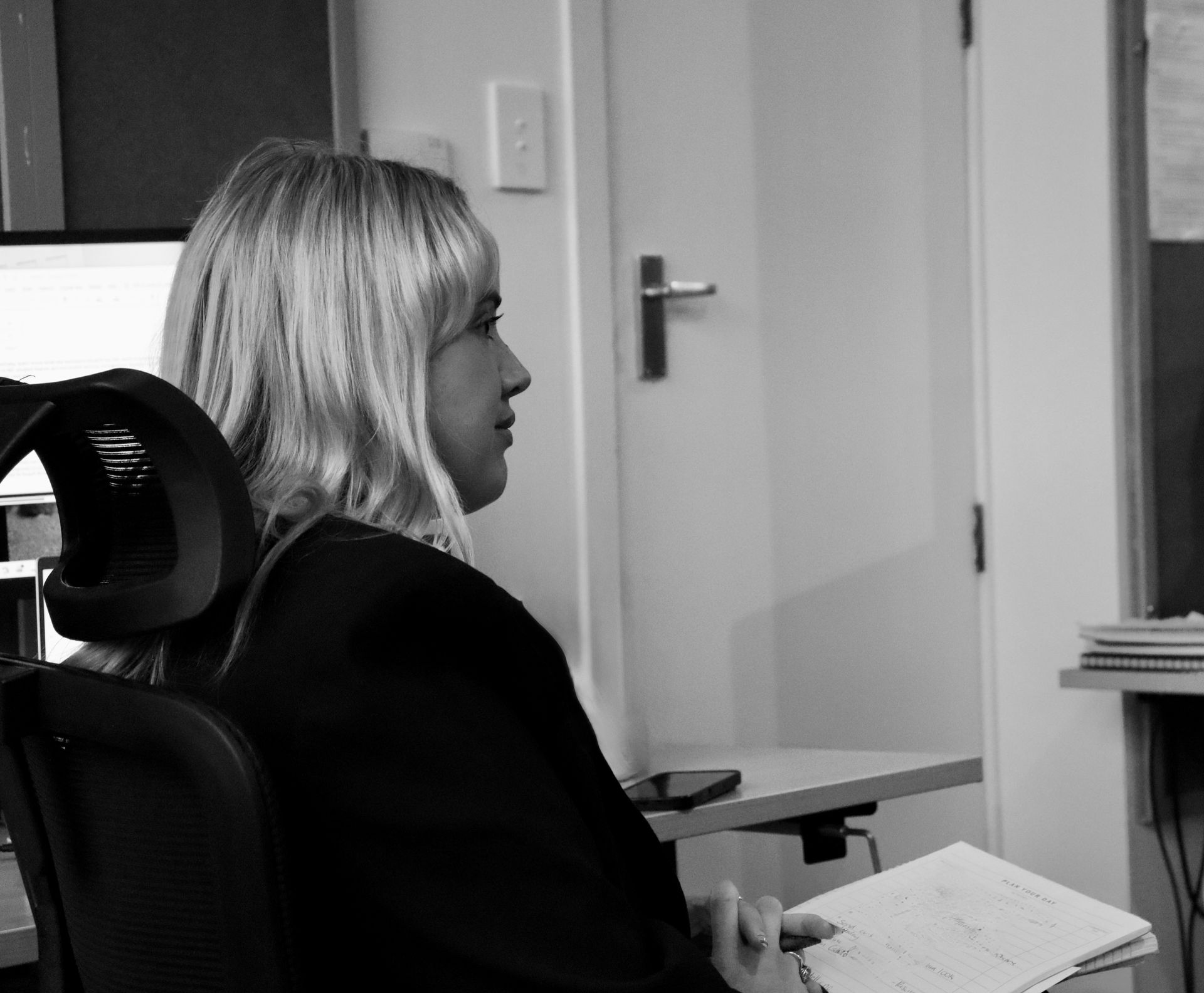 Two professionals meeting across a table in a bright office, one smiling and taking notes.