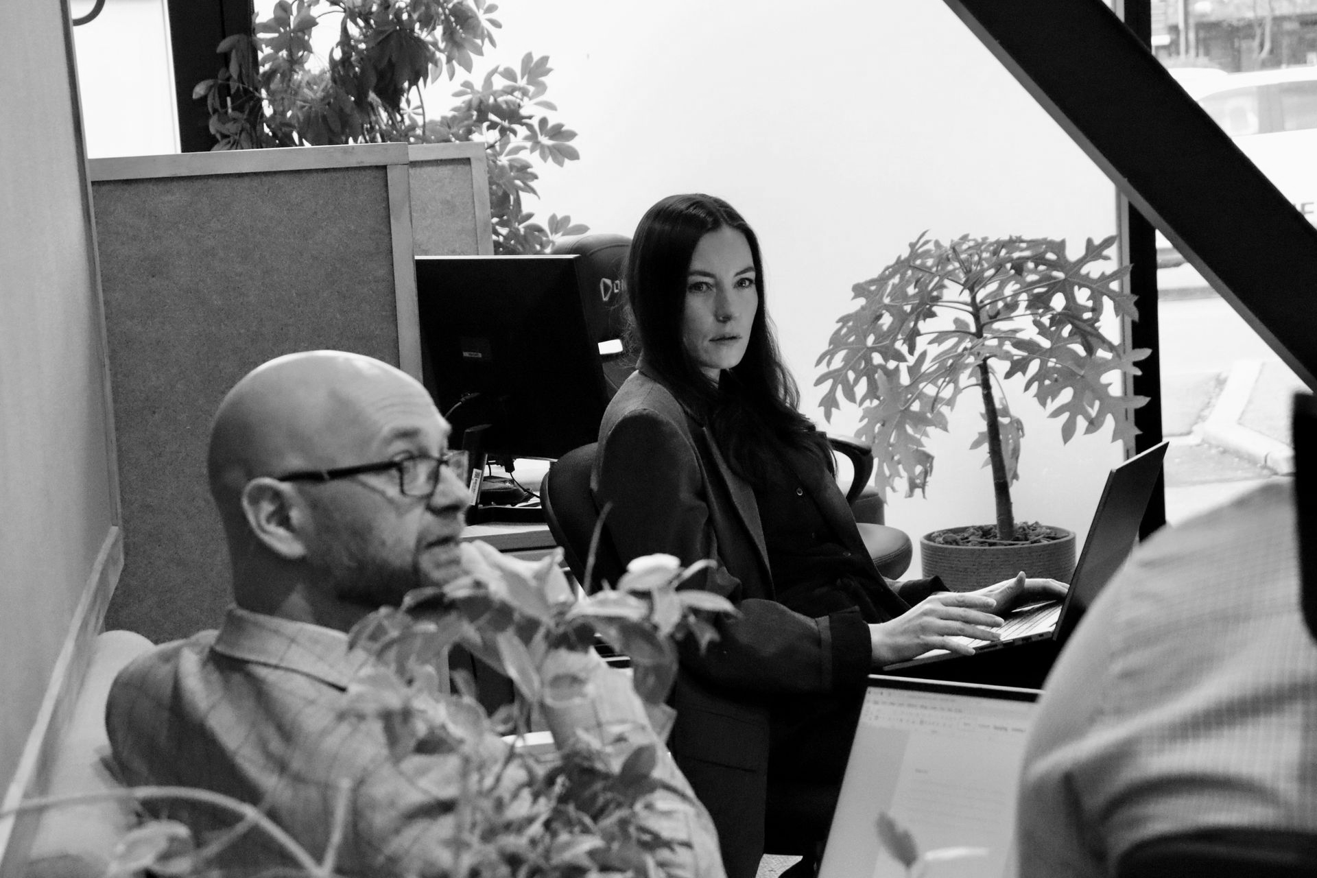 Person in an office meeting across a desk, reviewing documents on a laptop with notebooks and a plant nearby.