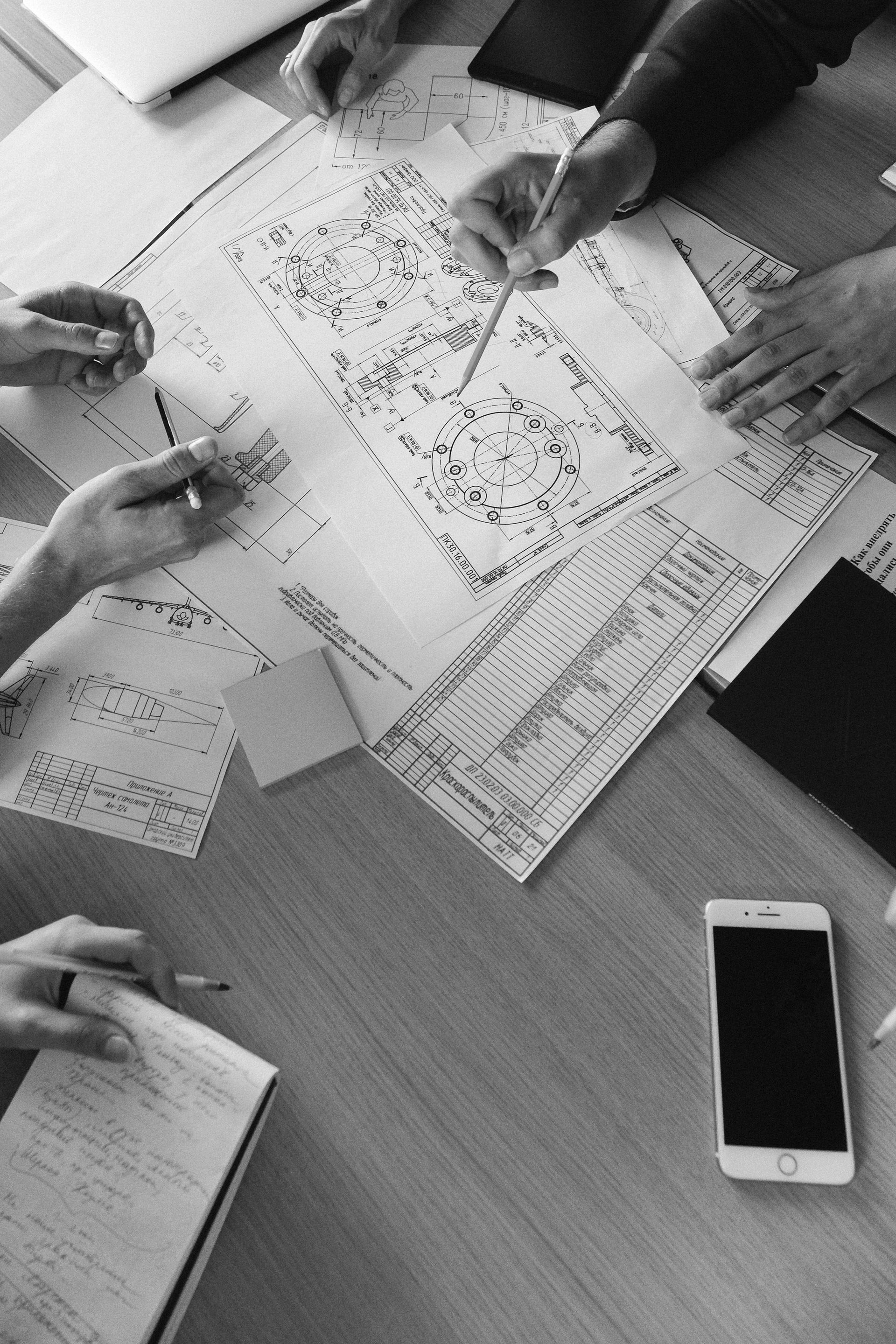 Hands reviewing papers around a table with a smartphone and notebook.