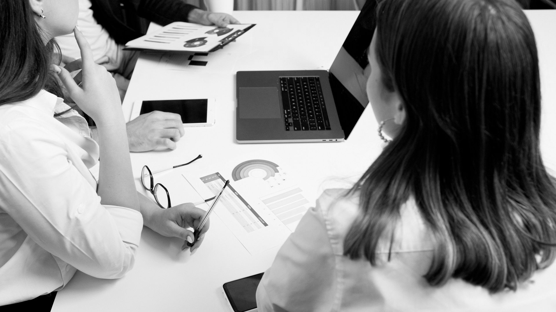 Two people in a meeting reviewing papers at a table with an open laptop.