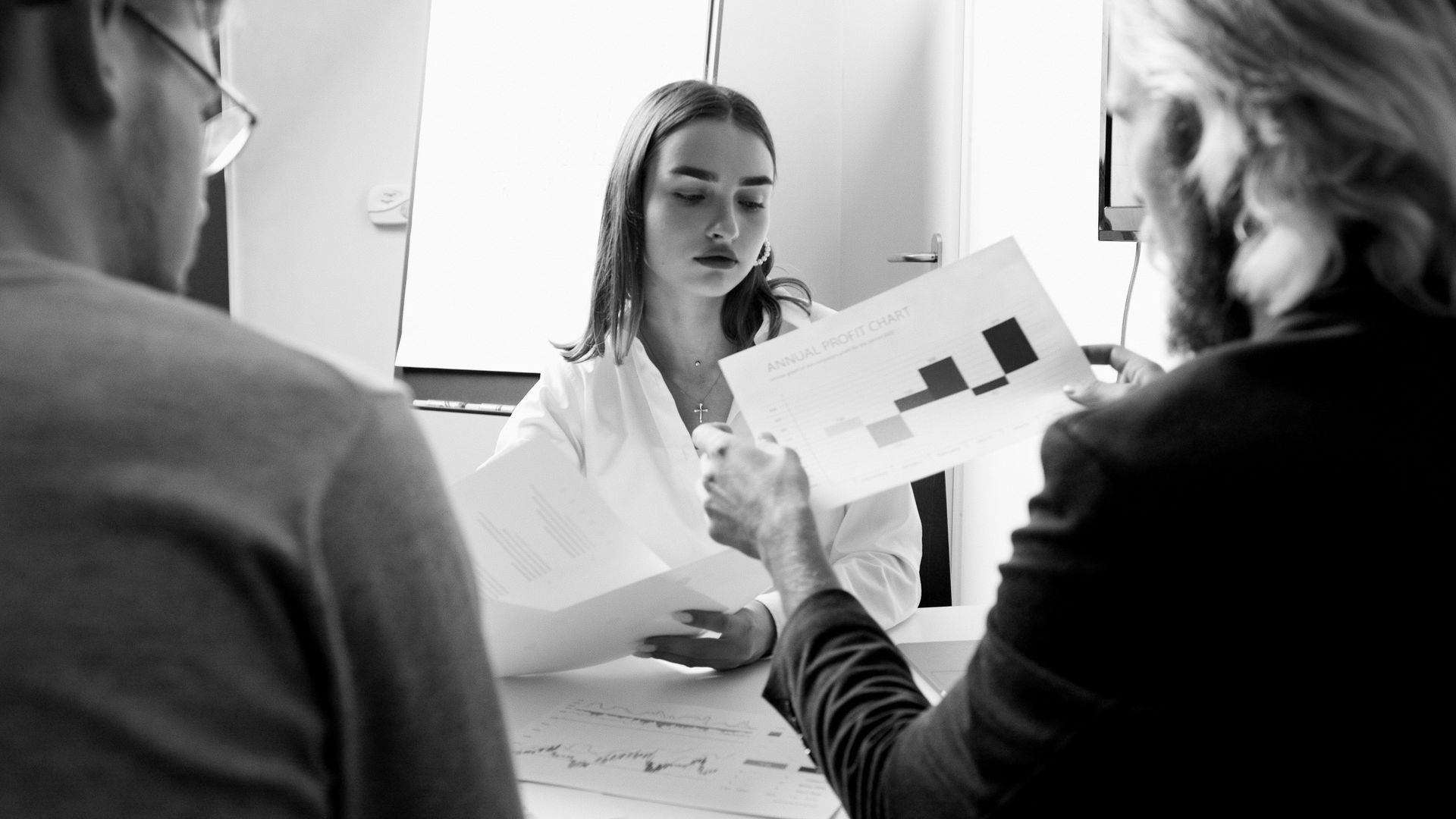 Three people in a meeting reviewing printed charts at a table